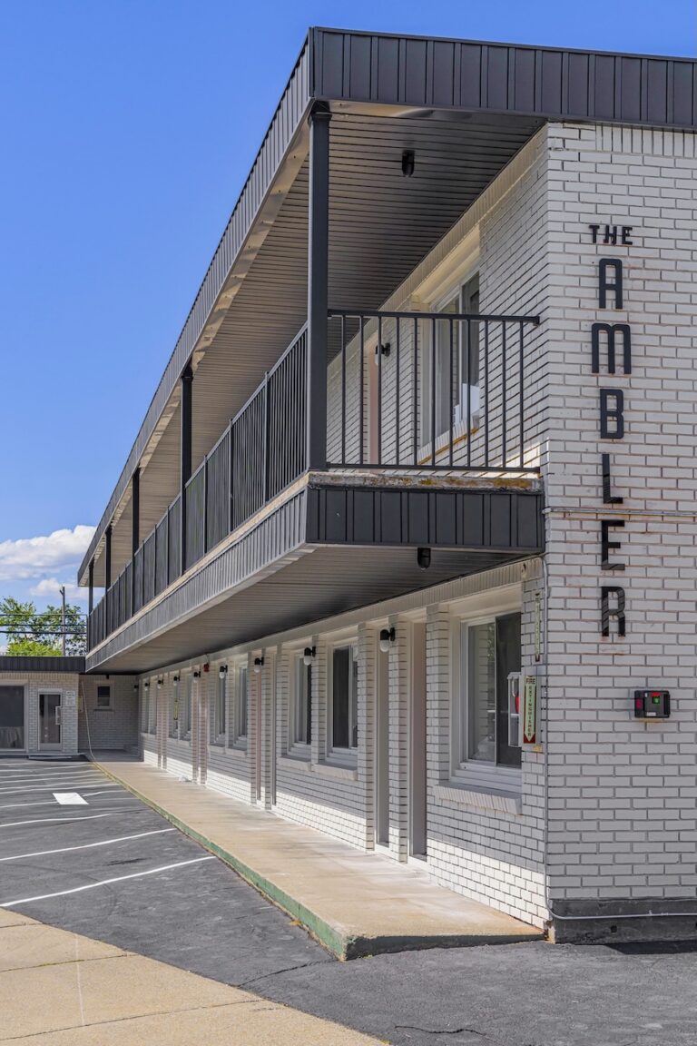 A two-story white brick motel with black railings, exterior doors and windows, and a sign reading 