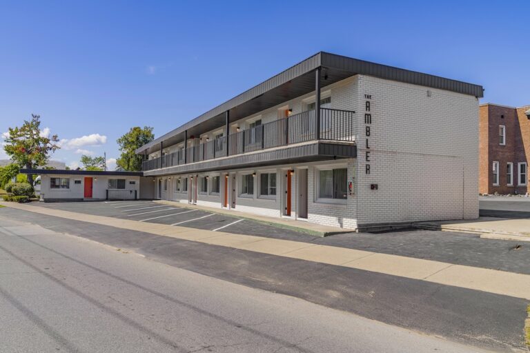 A two-story white brick motel with exterior corridors, black railings, and a sign reading 